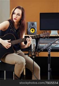 Photo of a beautiful brunette in a recording studio recording her guitar tracks.&#xA;