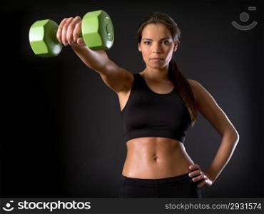 Photo of a beautiful female doing a front shoulder fly with a dumbbell over a dark background.