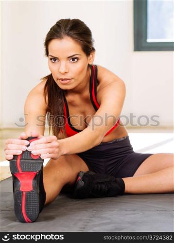 Photo of a beautiful female stretching on the floor sitting on a mat.