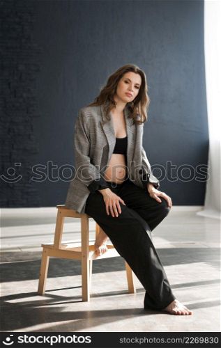 Photo of a beautiful pregnant woman with a bare stomach.. A pregnant girl with a bare stomach is sitting on a stepladder 4121.