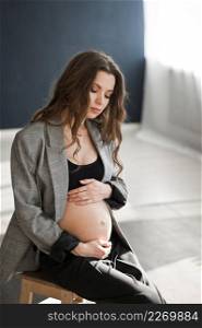 Photo of a beautiful pregnant woman with a bare stomach.. A pregnant girl with a bare stomach is sitting on a stepladder 4126.