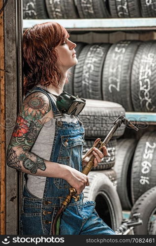 Photo of a beautiful redhead female mechanic with tattoos holding a welding torch.