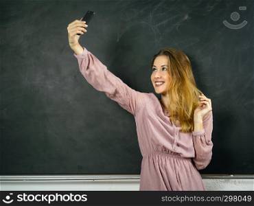 Photo of a beautiful student in a classroom doing a selfie in front of a blackboard.