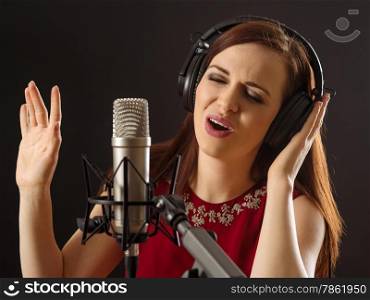 Photo of a beautiful woman singing into a large diaphragm microphone over dark background.