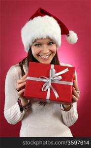 Photo of a beautiful young brunette female wearing a santa hat and holding a wrapped christmas gift.