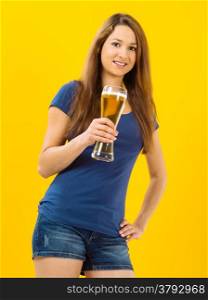 Photo of a beautiful young brunette woman drinking beer from a tall glass over yellow background.