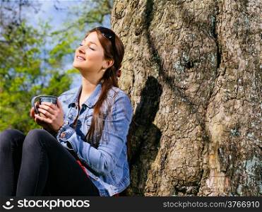 Photo of a beautiful young woman enjoying the warmth of the sun in early spring while she drinks her coffee.