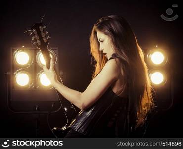 Photo of a beautiful young woman playing an electric guitar in front of stage lights.