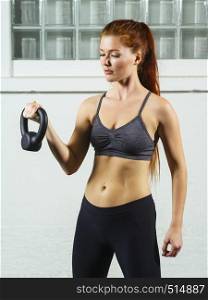 Photo of a beautiful young woman with red hair working out with kettlebell weights.