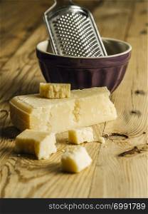 Photo of a block of parmesan cheese on a wooden table with grater in the background.