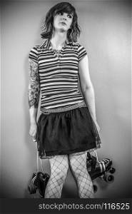 Photo of a bored roller derby girl holding her skates and waiting against a wall.