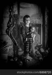 Photo of a creepy young boy holding an old clown doll in an old barn covered in spiderwebs and dust.