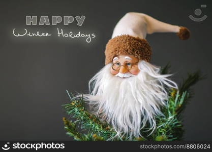 Photo of a decorative Santa Claus on a Christmas tree over gray background, festive greeting card with text space, happy winter holidays 