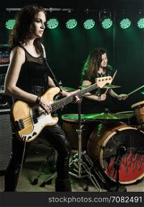Photo of a female bass player and drummer of a rock band playing on stage.
