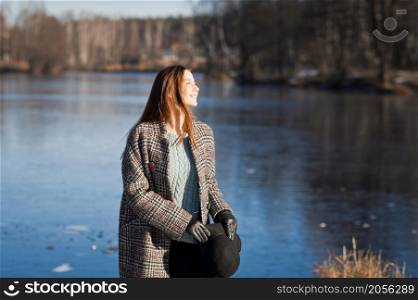 Photo of a girl in a hat and a half-coat against the background of melting snow.. A joyful girl against the background of awakening nature in early spring 3485.