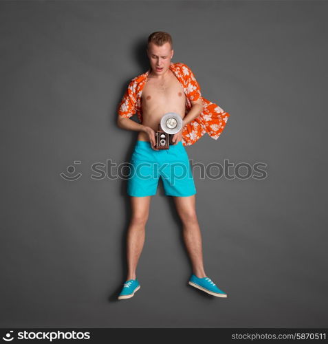 Photo of a male fashionable handsome hipster, taking picture with an old vintage photo camera with bulb flash on dark background.