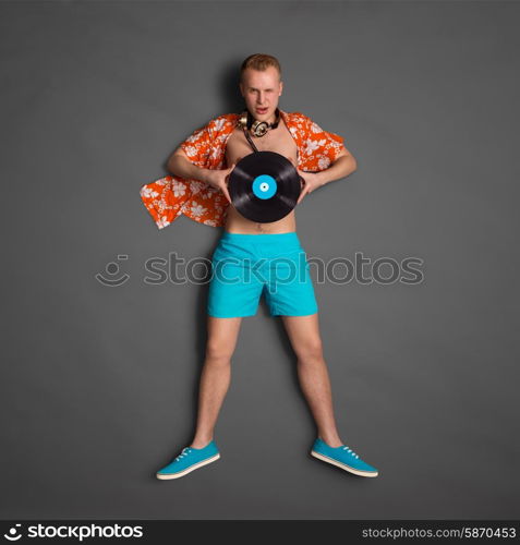 Photo of a male fashionable handsome hipster, wearing vintage music headphones around his neck and holding an LP microgroove vinyl record on dark background.