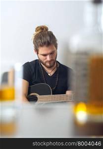 Photo of a male songwriter with acoustic guitar taken between a blurred whisky bottle and rocks glass.