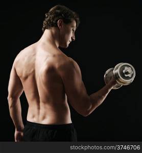 Photo of a man in his early thirties doing bicep curls with a dumbbell over a dark background. Rear view version.