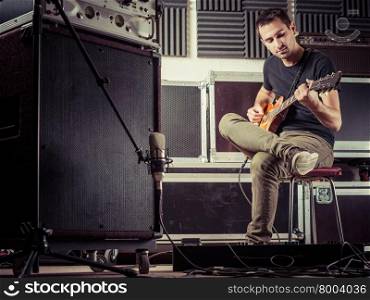 Photo of a man in his late 20&apos;s sitting in a recording studio recording his guitar tracks.