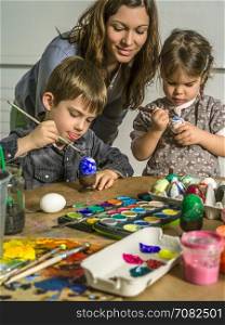 Photo of a mother and her children painting and decorating hard-boiled eggs for easter.