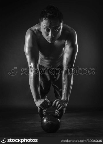 Photo of a muscular Asian man doing pushups with a kettlebell. Focus on his face.. Muscular man doing pushups with kettlebell