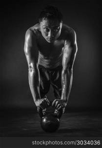 Photo of a muscular Asian man doing pushups with a kettlebell. Focus on his face.. Muscular man doing pushups with kettlebell