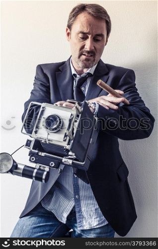 Photo of a photographer in his forties with an old 4x6 camera and holding a cigar. Filtered for more retro feel.
