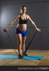 Photo of a pregnant woman in her thirties exercising with a resistance band.