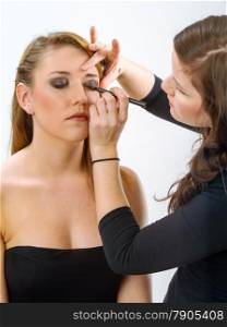 Photo of a professional makeup artist applying eye makeup onto a blond model.&#xA;