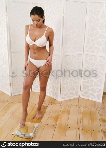 Photo of a slim young woman in her underwear about to step on a scale.&#xA;