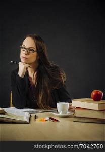 Photo of a teacher or business woman in her 30&rsquo;s sitting at a desk in front of a large blackboard.
