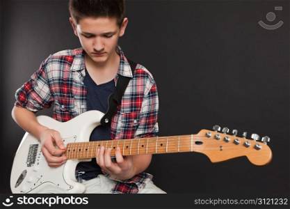 Photo of a teenage male playing a white electric guitar.