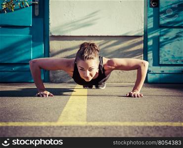 Photo of a toned young woman outside on the pavement doing pushups late in the day.&#xA;