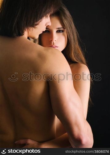 Photo of a topless young woman and man in love and holding each other. Woman is staring at the camera.