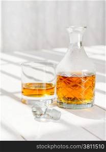 Photo of a whisky decanter and rocks glass on a table by a window.