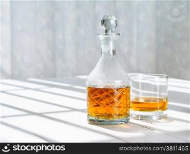 Photo of a whisky decanter and rocks glass on a table by a window.&#xA;