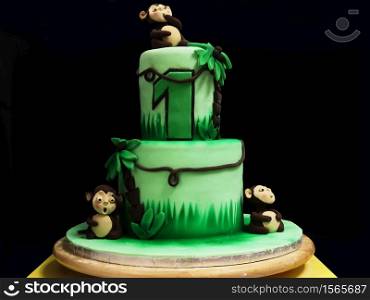 Photo of a whole green marzipan cake on a black background with monkeys, palm trees, coconut nuts and creepers.. Photo of a whole green marzipan cake on a black background