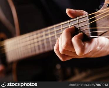 Photo of a woman playing an acoustic guitar with extreme shallow depth of field with focus on hand and headstock.