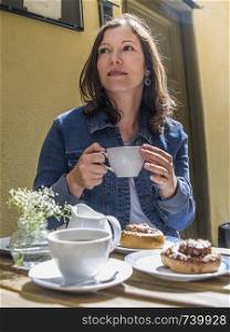 Photo of a woman sitting at an outdoor cafe in Gamla Stan, Stockholm, Sweden eating Kanelbulle and drinking coffee.