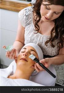 Photo of a young beautiful girl receiving a green facial mask in spa beauty salon.&#xA;