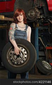 Photo of a young beautiful redhead mechanic wearing overalls and holding a wheel. Attached property release is for arm tattoos.