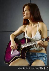 Photo of a young beautiful redhead woman sitting playing an acoustic guitar.
