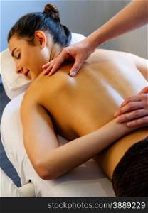 Photo of a young beautiful woman receiving a back massage from a professional masseuse. Focus on the hand of the therapist.
