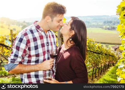 Photo of a young couple kissing and drinking wine in a vineyard.&#xA;