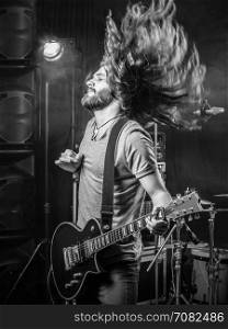 Photo of a young man playing electric guitar on stage and tossing his long hair around.