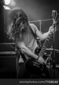 Photo of a young man playing electric guitar on stage and tossing his long hair around. Blurred motion with double exposure.