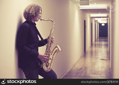 Photo of a young man playing the saxophone in a hallway. Heavily filtered.&#xA;