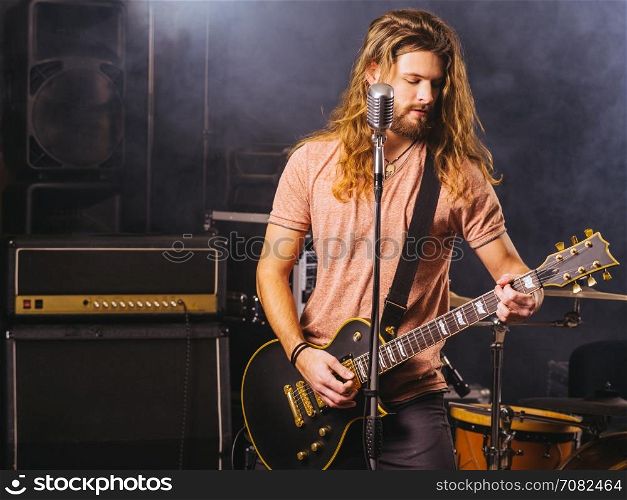 Photo of a young man with long hair and beard playing electric guitar on stage.