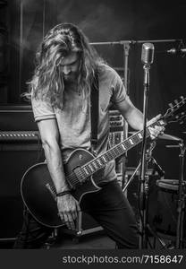 Photo of a young man with long hair playing electric guitar on stage.